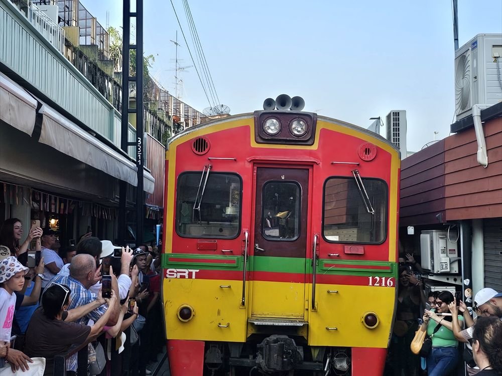 Travellers watching the train pass through a market in Thailand