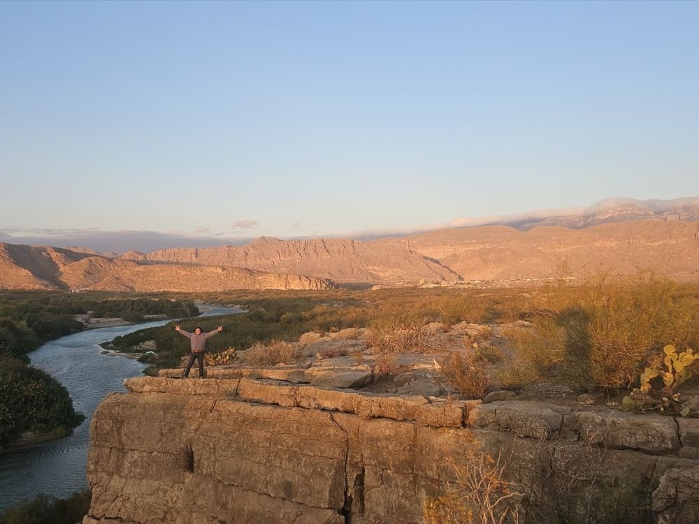 A traveller standing on a lookout above a canyon at sunset