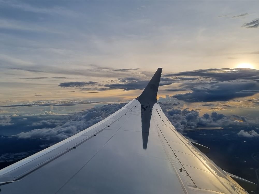 An aircraft wing above a sea of clouds at sunrise